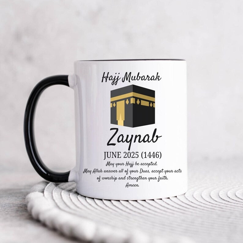 Black-handled Hajj Mubarak mug featuring Kaaba illustration, custom name "Zaynab," and an Islamic prayer for Hajj completion.