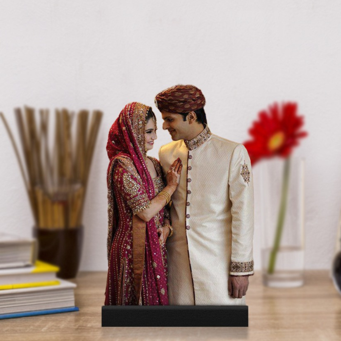 Personalized couple caricature of a bride in a red lehenga and groom in a sherwani, displayed on a wooden surface with a red flower and books in the background
