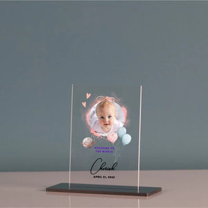 Custom baby photo acrylic plaque with newborn welcome sign, featuring a baby portrait and name, on a nursery shelf