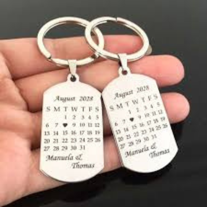 A pair of custom engraved silver keychains featuring a calendar design with a highlighted date and personalized names, making it a sentimental gift for couples, anniversaries, or special occasions.