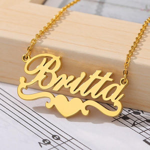 Customized name necklace in gold with the name "Britta" and a heart accent, displayed on a wooden surface with sheet music in the background