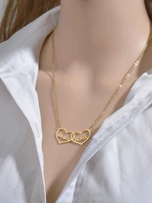 Customized name necklace in gold with "Laura" and "Nura" on heart pendants, worn on a white shirt with long brown hair visible