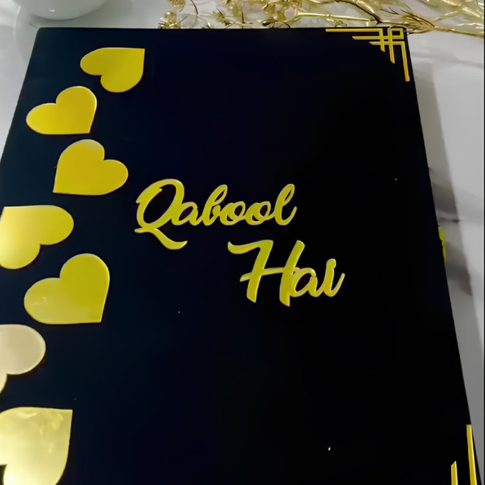 Customized Nikah velvet book kit with "Qabool Hai" text, featuring gold heart accents and a decorative Nikkah pen with feathers, displayed on a black velvet surface