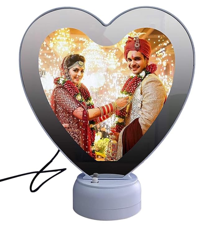 Heart shape LED magic mirror photo frame with a wedding photo of a bride in a red lehenga and groom in a sherwani, with festive lights in the background