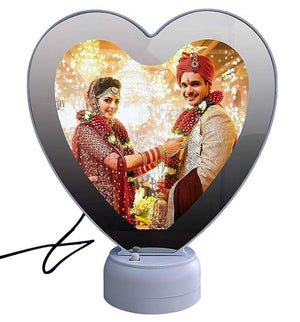 Heart shape LED magic mirror photo frame with a wedding photo of a bride in a red lehenga and groom in a sherwani, with festive lights in the background