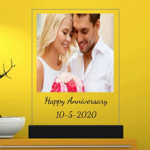 Personalized anniversary night lamp with "Happy Anniversary 10-5-2020" message, featuring a couple with flowers against a yellow background, placed on a wooden table
Notes