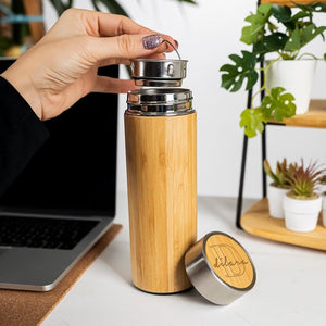 Personalized bamboo stainless steel tumbler with tea infuser and engraved lid, set on a desk next to a laptop and plants