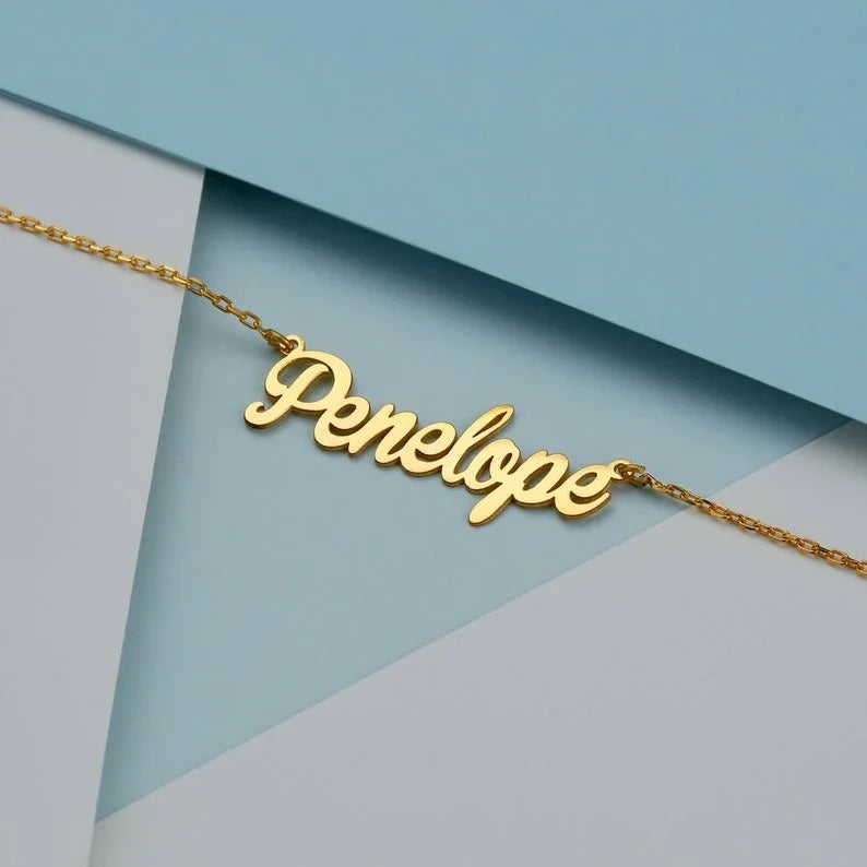 Personalized jewelry name necklace in gold with the name "Penelope," laid flat on a geometric blue and white background