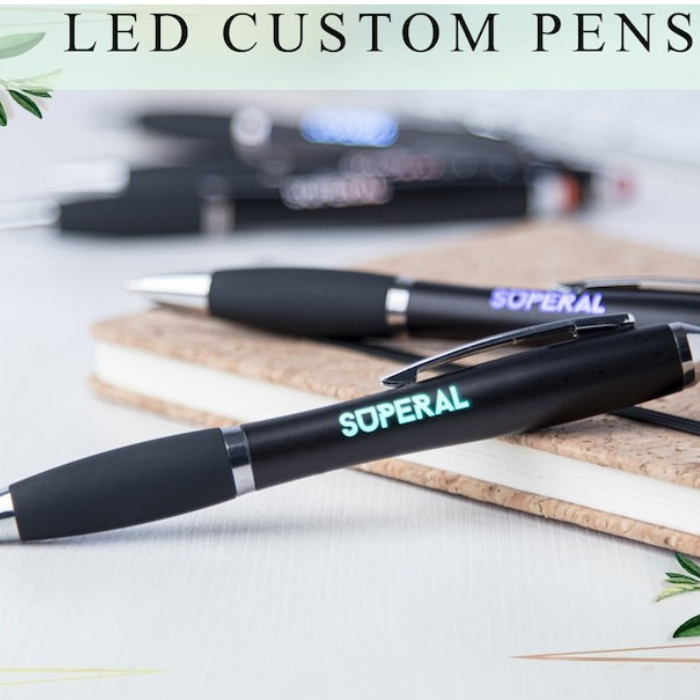 Close-up shot of LED custom pens with "SUPERAL" text glowing, placed on a notebook.