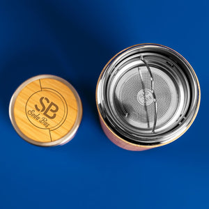 Close-up shot of a personalized bamboo tumbler with a stainless steel tea infuser and engraved lid, set against a simple, clean background.