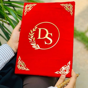 Elegant red velvet Nikkah booklet with gold acrylic initials and intricate gold corner embellishments, perfect for preserving an Islamic wedding certificate.