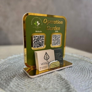 A green and gold Operation Garden QR Code Payment Sign with a business card holder, featuring QR codes for website access and digital payments via Zelle.