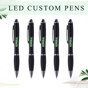A sleek black LED custom pen with engraved personalized text glowing in different colors, placed on a desk with notebooks in the background.