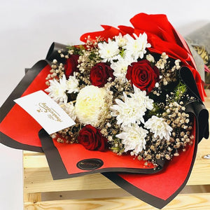Romantic red roses and white chrysanthemums bouquet wrapped in luxurious black and red paper with gold accents