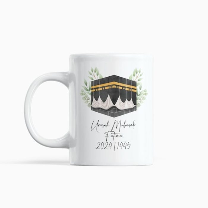 A sleek and minimalist white mug with an Umrah Mubarak design, showcasing the Kaaba in elegant artwork, customized with a name and Islamic year. A perfect keepsake for pilgrims.