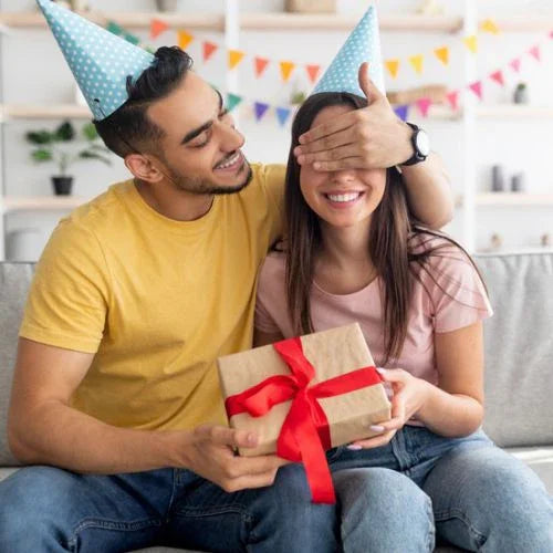 Man surprising woman with gift box, party hats, colorful bunting—perfect for birthdays or Nikah gifts