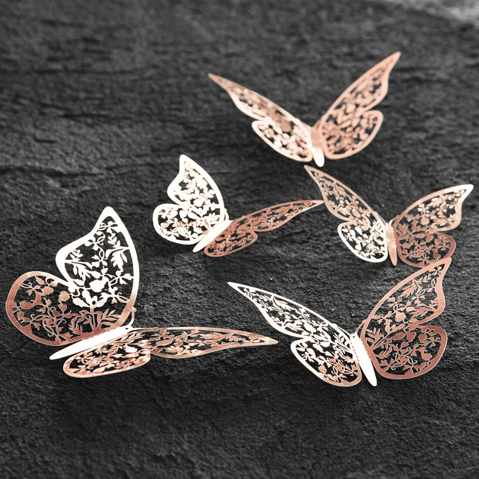 Elegant butterfly wall decor in rose gold metal, 3D butterfly wall art with delicate floral cut design on dark textured background.