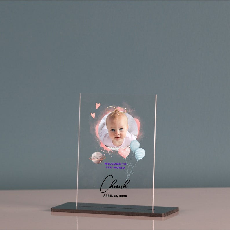 Custom baby photo acrylic plaque with newborn welcome sign, featuring a baby portrait and name, on a nursery shelf