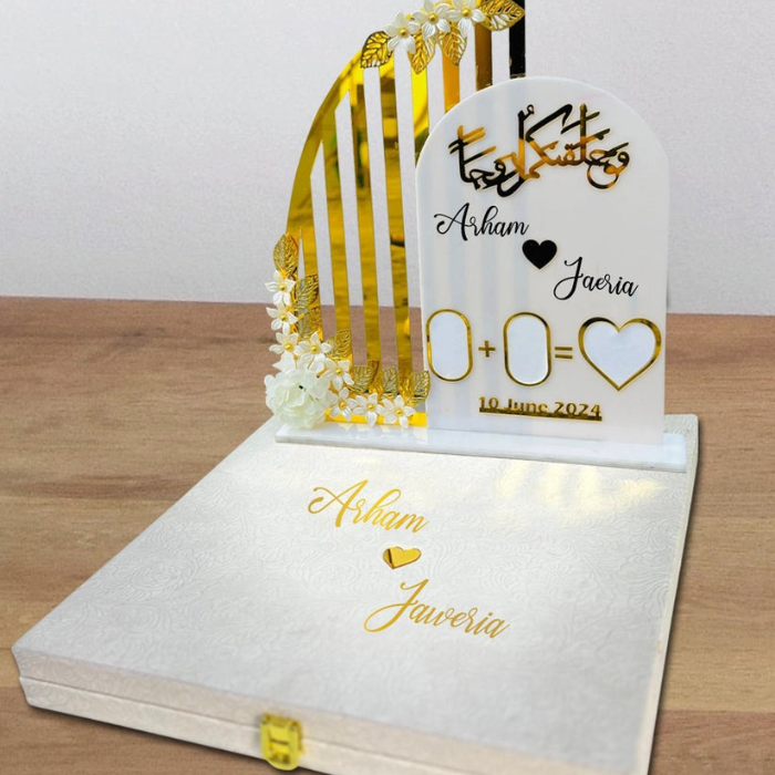 Personalized acrylic Nikkah thumb board with "Arham & Jaeria" and "10 June 2024," featuring floral accents and gold heart, in a velvet box on a wooden surface