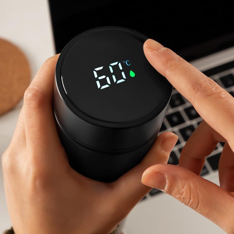  Close-up of a hand adjusting the digital temperature display on a custom black thermos, showing the temperature in degrees.