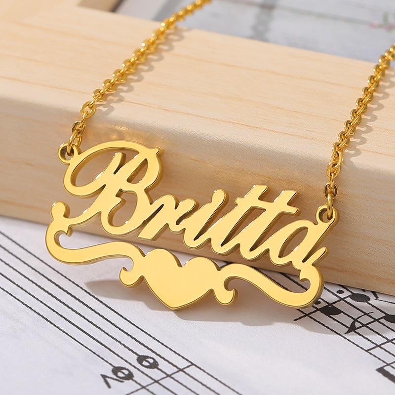 Customized name necklace in gold with the name "Britta" and a heart accent, displayed on a wooden surface with sheet music in the background