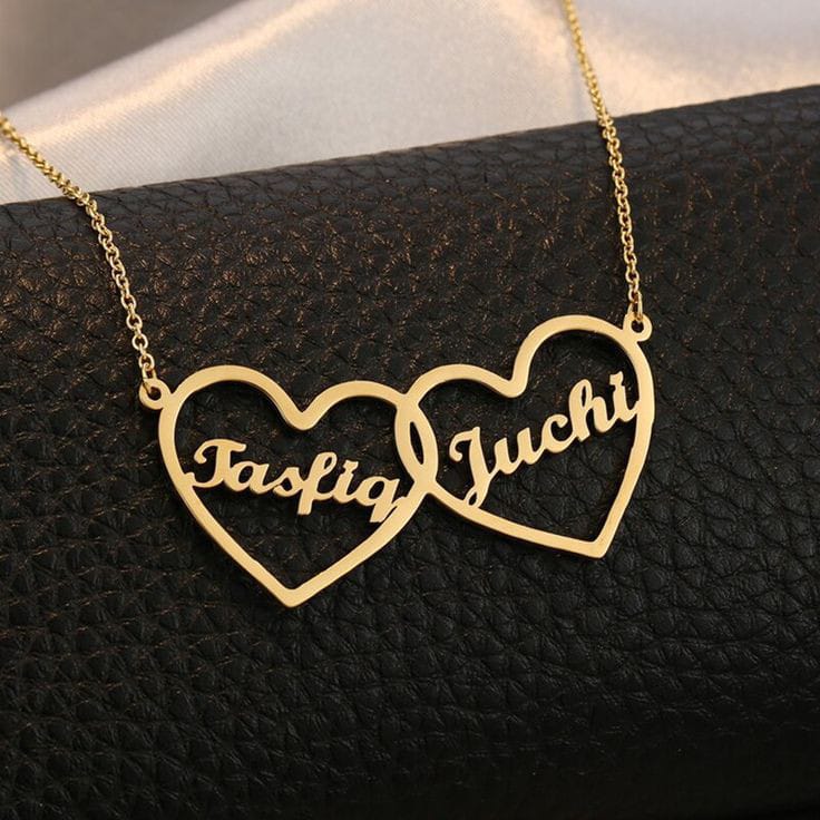 Customized name necklace in gold with "Tasfiq" and "Juchi" on heart pendants, displayed on a black textured surface