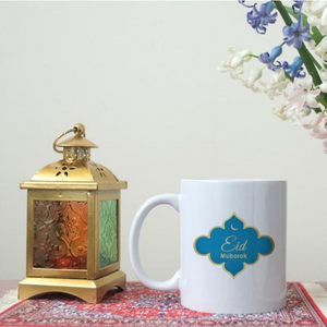  Eid Mubarak Mug with blue and gold design, placed next to a decorative lantern on a red-patterned tray.