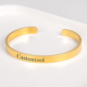 Engraved cuff bangle bracelet in gold with the word "Customized," displayed on a white surface