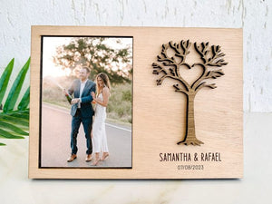Custom engraved wooden photo frame with a laser-cut tree and heart design, personalized with the names 'Samantha & Rafael' and their engagement date, holding a 4x6 photo of the couple celebrating."