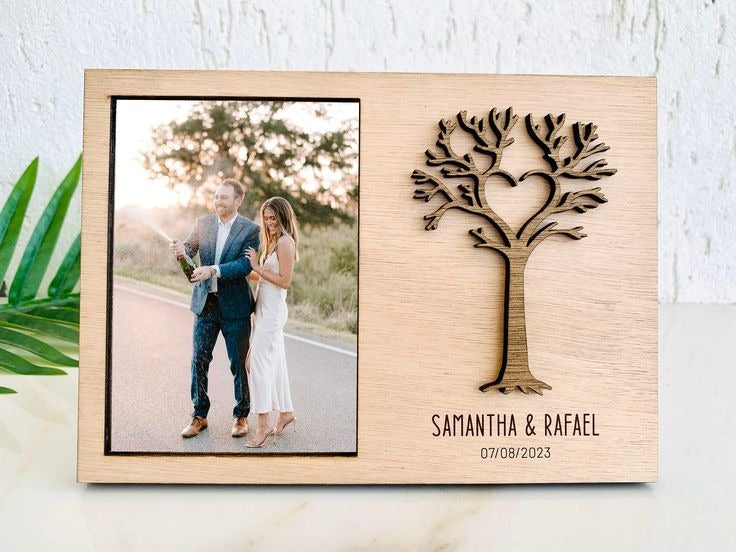 Custom engraved wooden photo frame with a laser-cut tree and heart design, personalized with the names 'Samantha & Rafael' and their engagement date, holding a 4x6 photo of the couple celebrating."