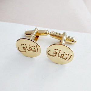 Closeup of personalized gold cufflinks with the Arabic name "Itfaq" engraved, displayed on a white background