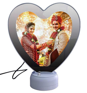 Heart shape LED magic mirror photo frame with a wedding photo of a bride in a red lehenga and groom in a sherwani, with festive lights in the background
