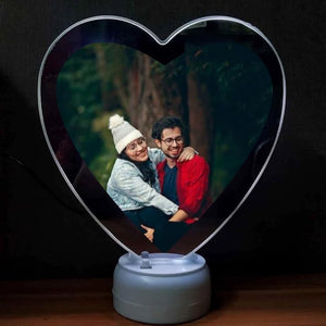 Heart shape LED magic mirror photo frame with a casual couple photo in a forest setting, displayed on a wooden surface
