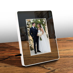 LED magic mirror photo frame with a wedding photo of a bride and groom, displayed on a wooden table with a plant in the background