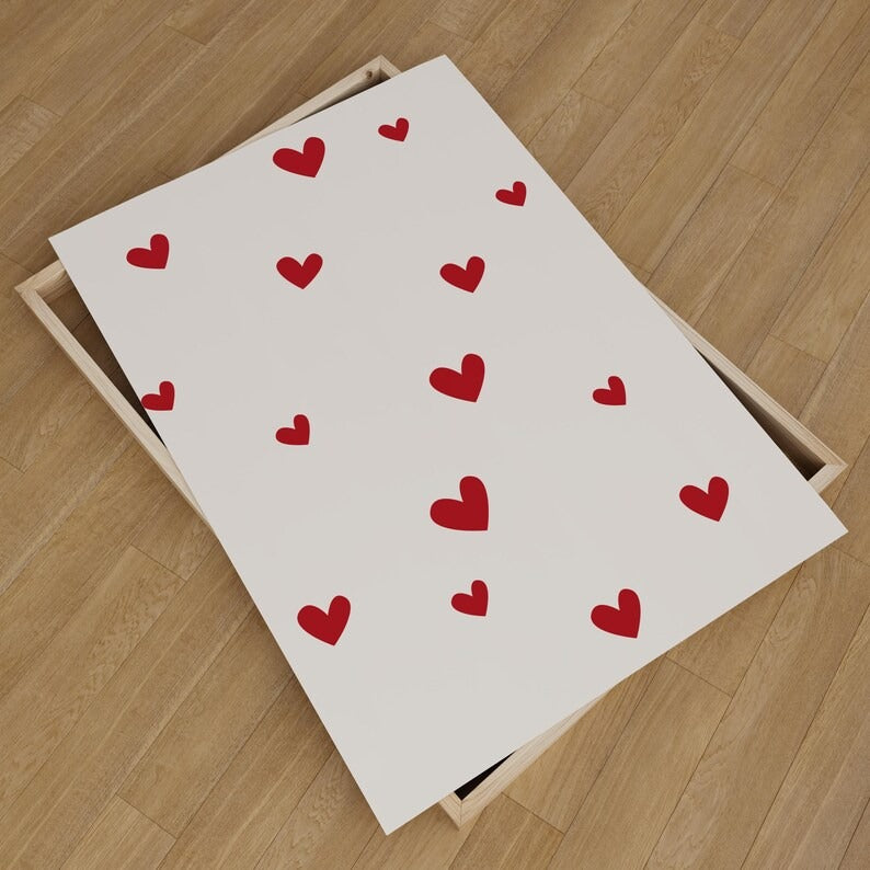 Minimalist red hearts wall art print unboxed on a wooden floor, featuring scattered heart patterns for romantic and modern home decor.