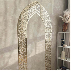 Mehrab wall art in gold with intricate geometric patterns, displayed on a beige wall with a shelf and decor elements in the background