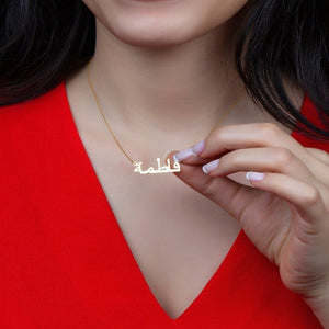 Customized name necklace in gold with the name "Fatima" in Arabic, worn on a red top with dark hair visible