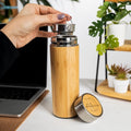 Personalized bamboo stainless steel tumbler with tea infuser and engraved lid, set on a desk next to a laptop and plants