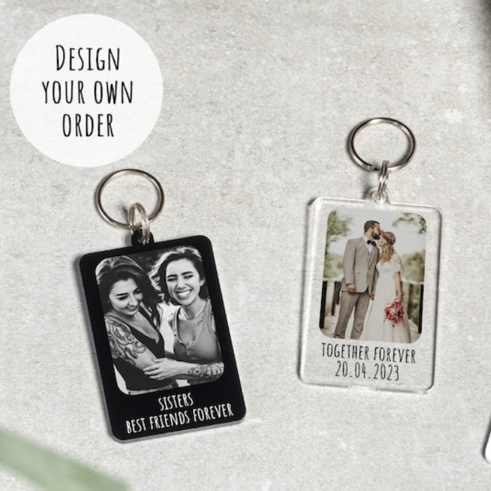  Two custom photo keyrings, one featuring a black-and-white picture of two smiling sisters with the text "Sisters Best Friends Forever," and the other with a wedding couple captioned "Together Forever 20.04.2023."