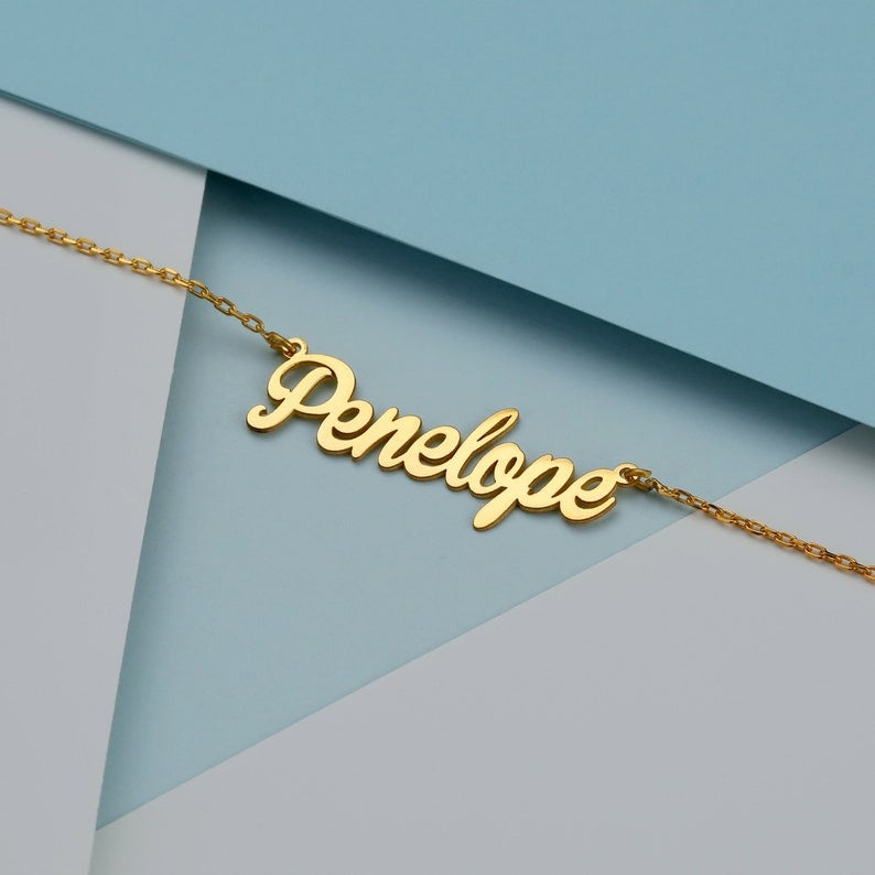 Personalized jewelry name necklace in gold with the name "Penelope," laid flat on a geometric blue and white background