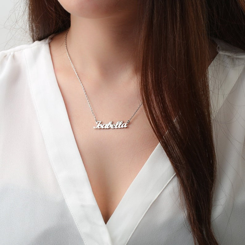 Personalized jewelry name necklace in silver with the name "Isabella," worn on a white shirt with long brown hair visible