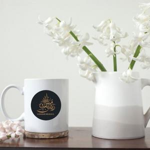 Close-up of Ramadan Mubarak mug with Arabic calligraphy, placed next to a vase with white flowers.