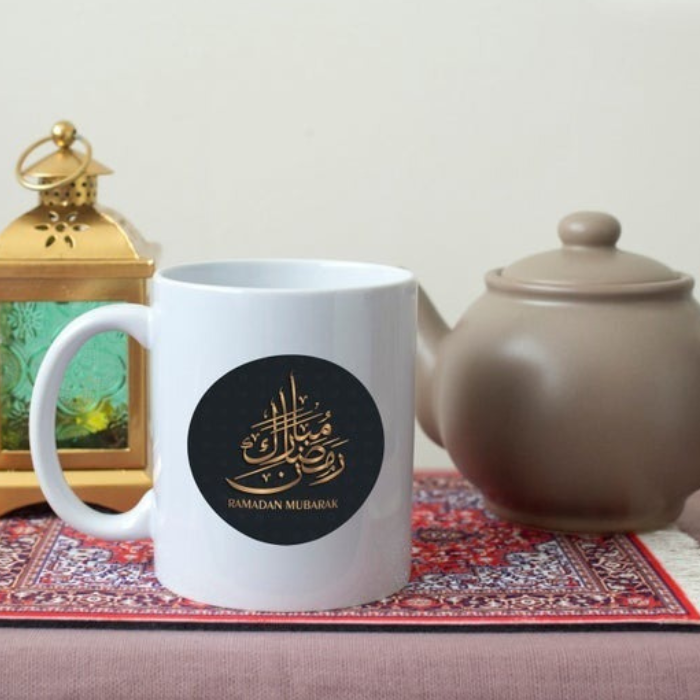 Ceramic Ramadan Mubarak Mug with elegant Arabic calligraphy, placed on a table with Ramadan-themed decor.
