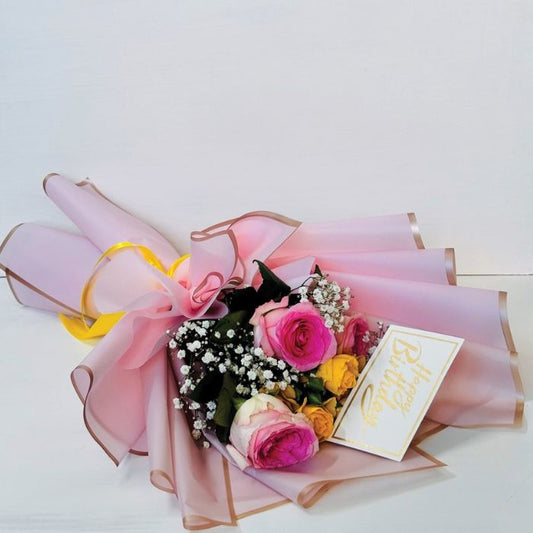 Elegant mixed rose birthday bouquet with pink and yellow roses wrapped in sheer pink paper and golden accents.