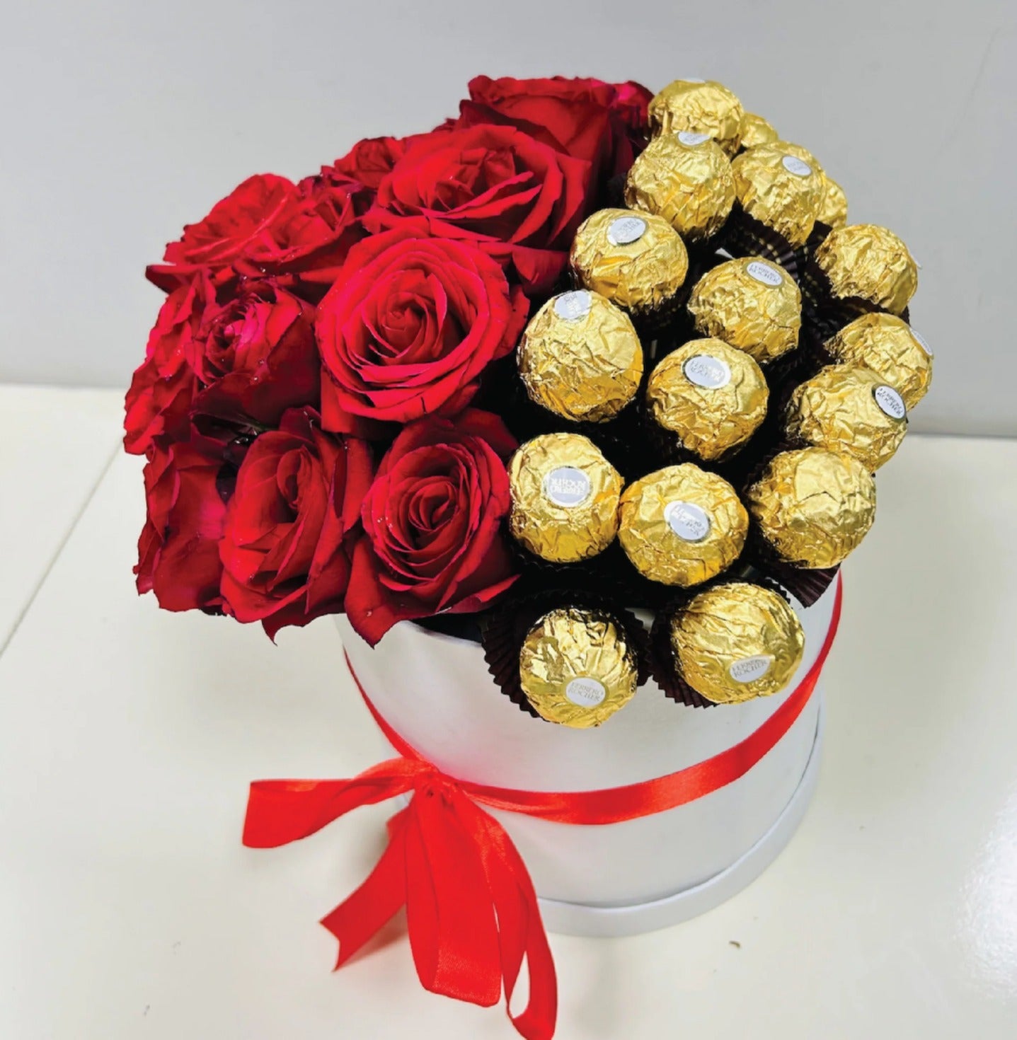 Luxury white gift box with red roses and Ferrero Rocher chocolates, tied with a red satin ribbon, perfect for romantic gifting.