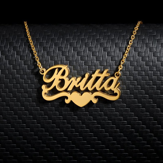 Customized name necklace in gold with the name "Britta" and a heart accent, displayed on a black surface 