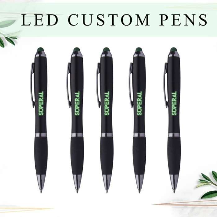 A sleek black LED custom pen with engraved personalized text glowing in different colors, placed on a desk with notebooks in the background.