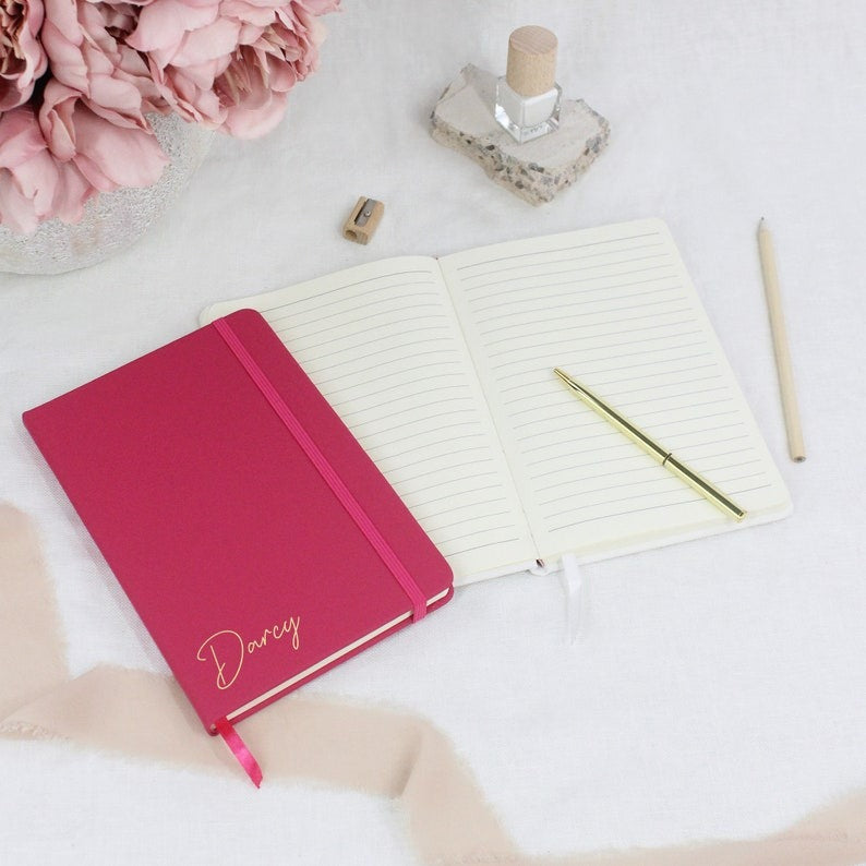 Stylish pink personalized notebook with lined pages, an elastic closure, and a bookmark ribbon.