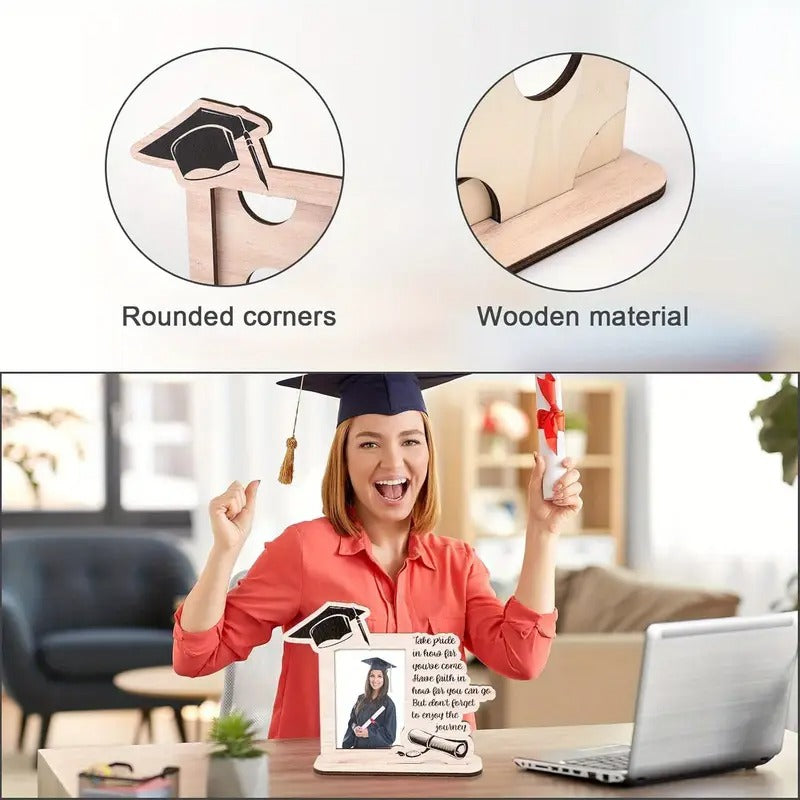 Graduate holding a wooden graduation photo frame with "Take Pride" quote and cap design, displayed indoors with a laptop and decor in the background